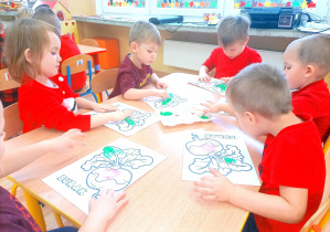Dzieci paluszkami malują liście zieloną farbą.