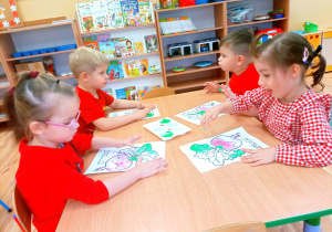 Dzieci przy stoliczku malują paluszkami maczanymi w zielonej farbie.