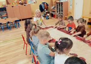 Przedszkolaki z nauczycielką mieszają rękami farbę przy stolikach.