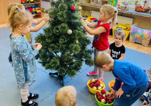 Sześcioro przedszkolaków dekoruje świąteczne drzewko.