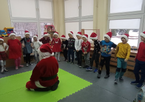 Mikołaj siedzi na dywanie i ogląda występ dzieci