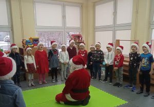 Mikołaj siedzi na dywanie i ogląda występ dzieci