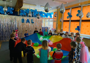 Dzieci trzymają chustę animacyjną, na której są kolorowe balony.