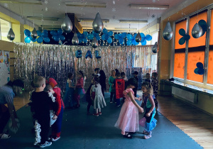 Przedszkolaki tańczą z balonami trzymając je między kolankami.