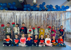 Przedszkolaki pozują do zdjęcia z czerwonymi sercami i kwiatami.