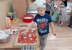 Sebastianek układa na pizzy wędlinę.