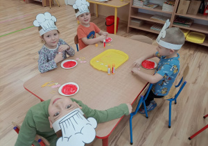 Czworo dzieci przy stoliku komponuje papierowe pizze.