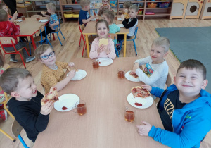 Przedszkolaki jedzą wspólnie wykonaną pizzę.