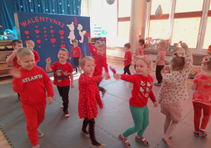 Dzieci podczas zabawy ruchowo-muzycznej spacerują po macie z sercami z papieru.