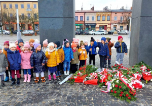 Dzieci z grupy III pozują do zdjęcia z boku widać złożone przed pomnikiem kwiaty