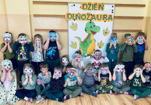 Grupa przedszkolaków pozuje do zdjęcia we własnoręcznie wykonanych maskach dinozaurów.