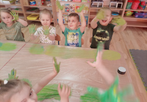 Dzieci śmieją się do zdjęcia pokazując rączki pomalowane zieloną farbą.