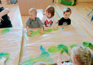 Dzieci łączą niebieską i żółtą farbę za pomocą rączek.