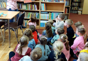 Dzieci z uwagą słuchają bajki czytaną przez panią z biblioteki