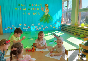 Dzieci kolorują przy stolikach portret Pani Wiosny