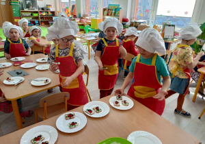 Trzech chłopców układa wykonany przez siebie deser na talerzykach.