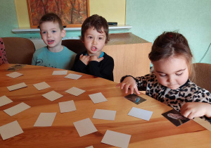 Dzieci siedzą przy stole przed nimi rozłożone karty do gry w memory