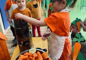 Milenka wkłada marchewkę do wyciskarki.