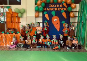 Przedszkolaki pozują na tle dekoracji z kubeczkami i marchewkami.