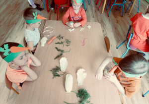 Dzieci przy stoliczku z przygotowanymi materiałami do tworzenia warzywnych ludzików.