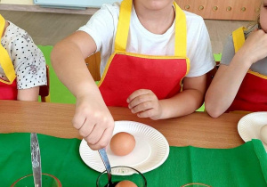 Igorek wkłada jajo do kubka z barwnikiem