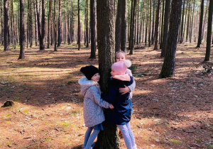 Dziewczynki przytulają drzewo.