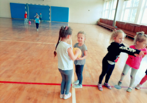 Dzieci na sali gimnastycznej podczas zabaw z piłką w małych grupach.