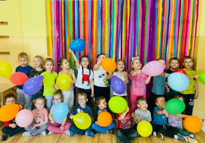 Dzieci na tle dekoracji machają kolorowymi balonami.