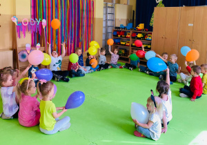 Przedszkolaki siedzą w kole z balonami.