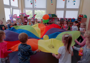 Uśmiechnięte przedszkolaki podrzucają balony na chuście animacyjnej.