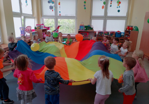 Przedszkolaki podrzucają balony na chuście animacyjnej.