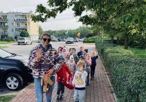 Dzieci wraz z nauczycielką spacerują trzymając jamniczka.