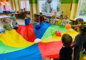 Przedszkolaki podrzucają kolorowe balony za pomocą chusty.
