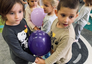 Przedszkolaki tańczą z balonami pomiędzy brzuszkami.