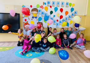 Przedszkolaki podrzucają balony przy dekoracji z okazji Dnia Przedszkolaka.