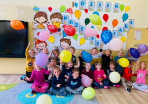 Przedszkolaki podrzucają balony przy dekoracji z okazji Dnia Przedszkolaka.