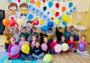 Przedszkolaki z balonami w rączkach ustawiły się przy dekoracji z okazji Dnia Przedszkolaka.