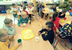Przedszkolaki po wspaniałej zabawie zjadają pyszne chrupki przy stoliczkach.