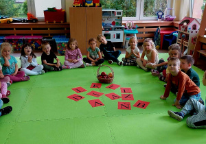 Dzieci siedzą w kole po środku rozłożone litery, które utworzą napi "DZIEŃ JABŁKA "