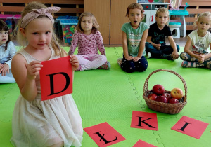 Dziewczynka trzyma w dłoni czerwoną kartkę z litera D