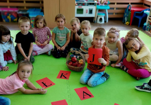 Dzieci siedzą w kole w środku czerwone kartki z literami