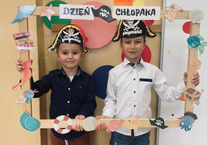 Dwóch chłopców w czapkach piratów pozują do zdjęcia w ramce z okazji Dnia Chłopaka.
