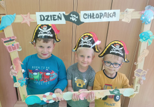 Trzech chłopców w czapkach piratów pozują do zdjęcia w ramce z okazji Dnia Chłopaka.