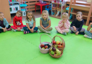 Dzieci siedzą w kole na środku przed nimi postawione są kosze z owocami