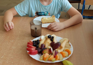 Chłopiec siedzie przy stole, na którym jest talerz z owocami