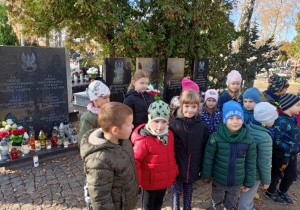 Grupa dzieci stojąca na tle grobów żołnierskich.