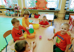 Dzieci bawią się z użyciem zabawkowych naczyń i sypkich produktów spożywczych.