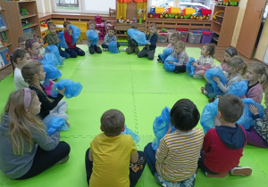 Dzieci siedzące w kole pocierające dłońmi o folię.