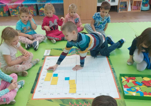 Chłopiec układa zielony kwadrat zgodnie z instrukcją nauczycielki