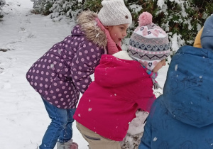 Troje dzieci toczy kulę ze śniegu.